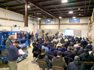 NE employees sitting in warehouse listening to a safety day presentation
