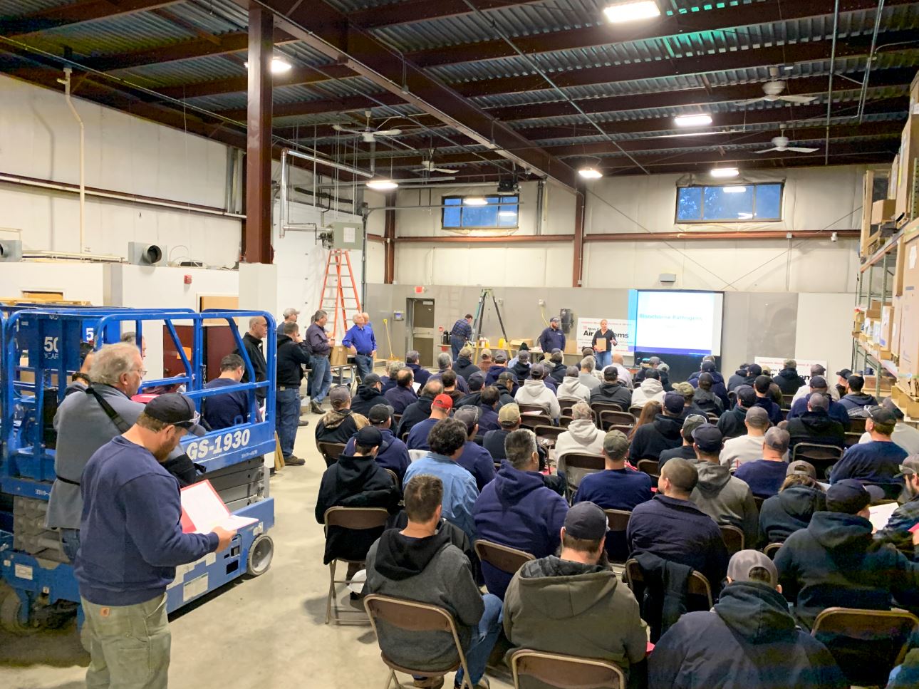 NE employees sitting in warehouse listening to a safety day presentation