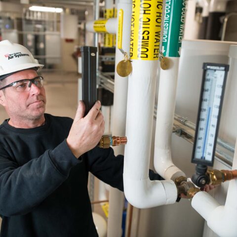 NE Air employee wearing hard hat performing service on HVAC plumbing